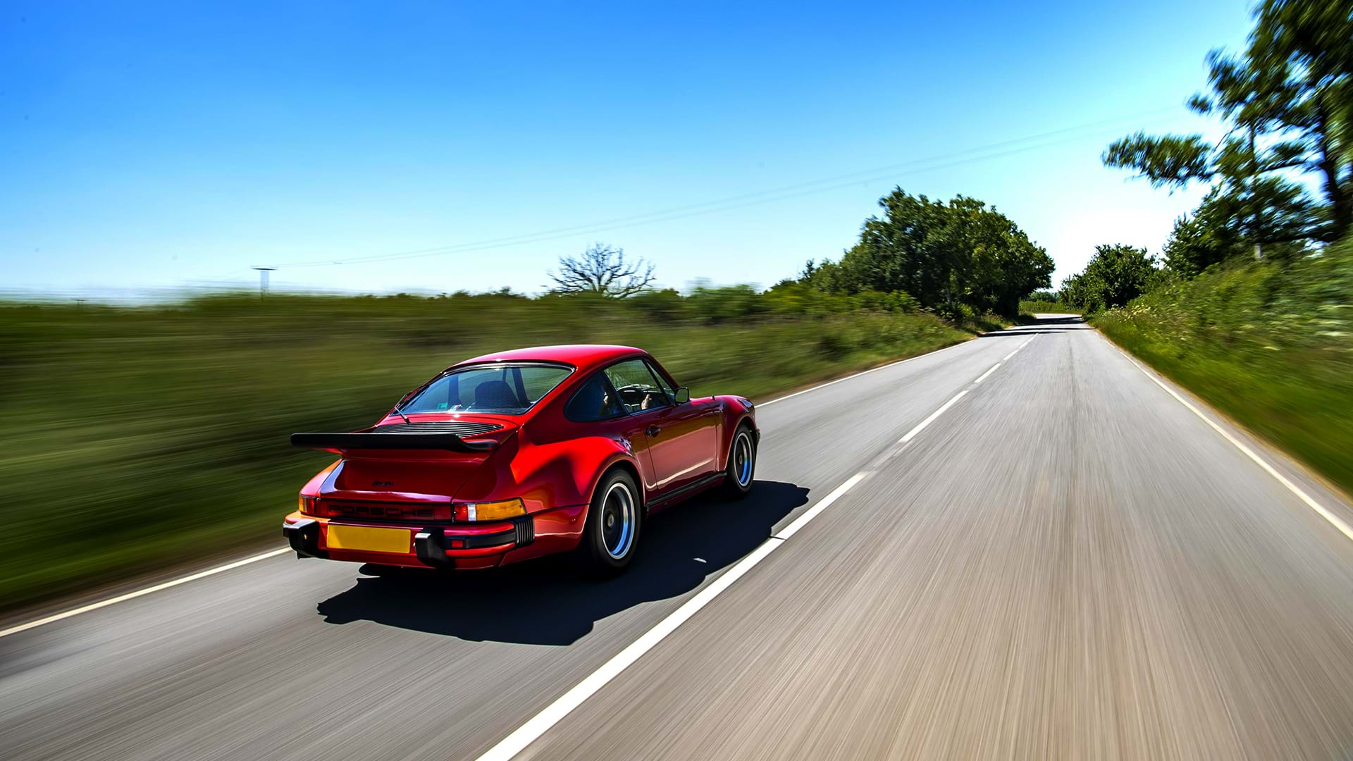 Rouge vintage Porsche 930 Turbo rugissant sur une belle route de campagne par une journée ensoleillée.
